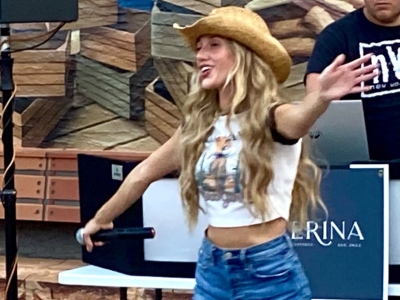 Woman in a cowboy hat and white crop top with blue jeans standing in front of stacked wooden planks.